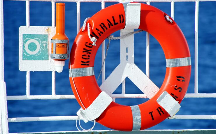 orange and white life buoy hanged on metal fence