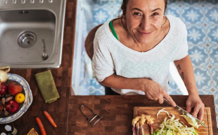 femme en chemise blanche à col rond tenant une planche à découper en bois marron sourire de cuisine