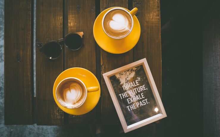 two coffee lattes in yellow cup with saucer on brown wooden table