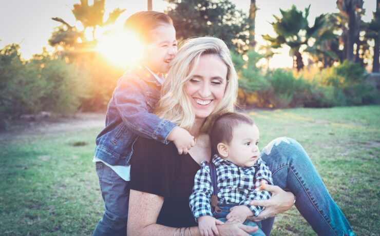 femme tenant un bébé assis sur un champ d'herbe verte sous le coucher du soleil