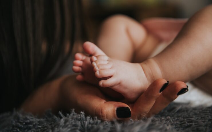 Les pieds d'un bébé sont tenus par la main d'une femme aux mains peintes et manucurées reposant sur une couverture grise