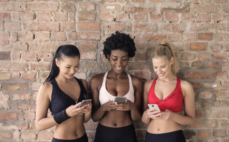 Three Woman in Assorted-color Sport Bras Holding and Watching Their Smartphones friends