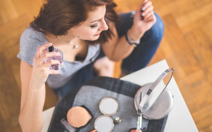 femme assise devant un miroir tenant une bouteille de parfum