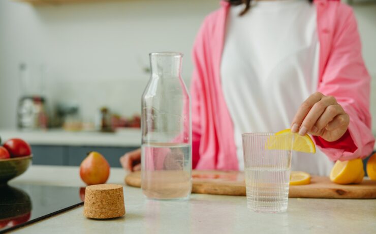 Femme mettant une rondelle de citron dans un verre d'eau dans la cuisine