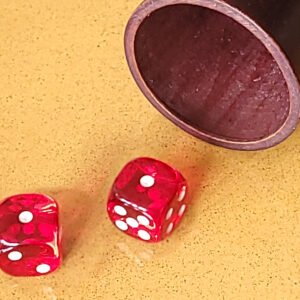 Deux dés rouges sur une surface jaune à côté d'une tasse en bois