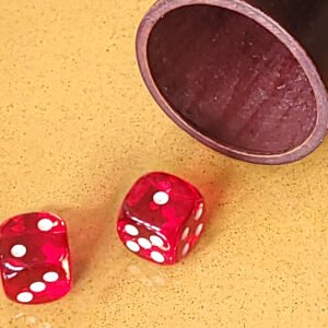 Deux dés rouges sur une surface jaune à côté d'une tasse en bois