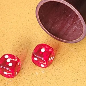 Deux dés rouges sur une surface jaune à côté d'une tasse en bois