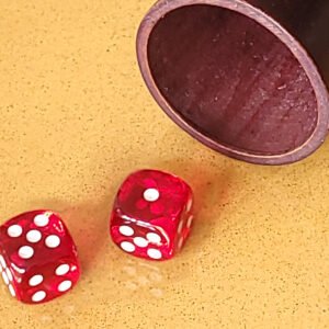 Deux dés rouges sur une surface jaune à côté d'une tasse en bois