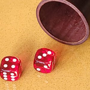 Deux dés rouges sur une surface jaune à côté d'une tasse en bois