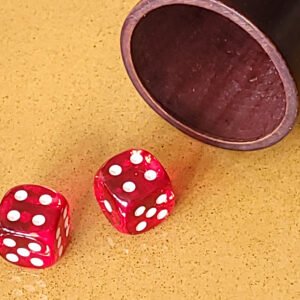 Deux dés rouges sur une surface jaune à côté d'une tasse en bois