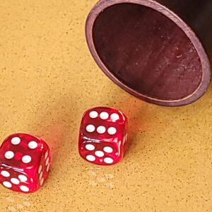 Deux dés rouges sur une surface jaune à côté d'une tasse en bois