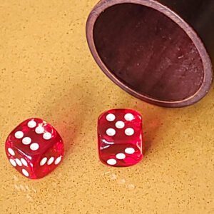 Deux dés rouges sur une surface jaune à côté d'une tasse en bois