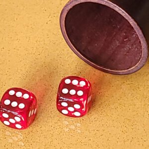 Deux dés rouges sur une surface jaune à côté d'une tasse en bois