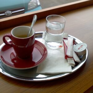tasse à café en céramique rouge avec un verre d'eau à côté sur un plateau en acier inoxydable