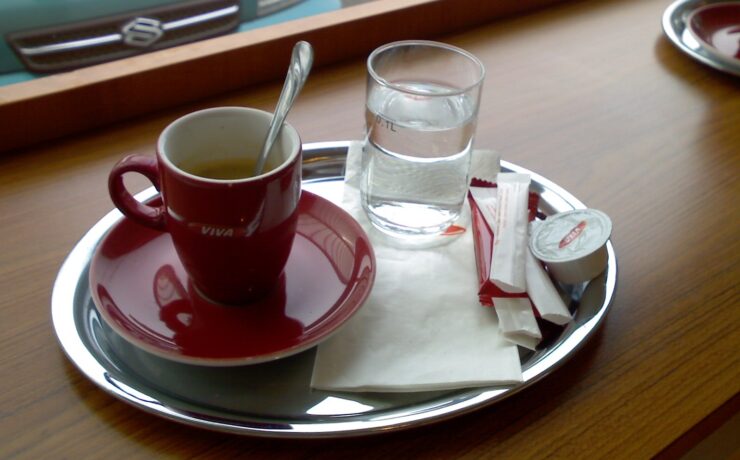 tasse à café en céramique rouge avec un verre d'eau à côté sur un plateau en acier inoxydable