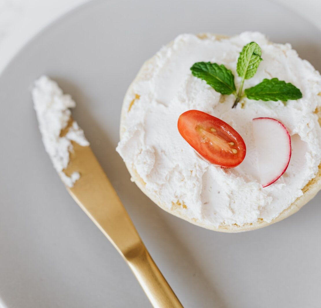 Vu du haut, une délicieuse tartinade de mascarpone sur du pain décoré de légumes et de menthe sur un plateau rond avec un couteau doré posé sur une table en marbre.