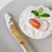 Vu du haut, une délicieuse tartinade de mascarpone sur du pain décoré de légumes et de menthe sur un plateau rond avec un couteau doré posé sur une table en marbre.