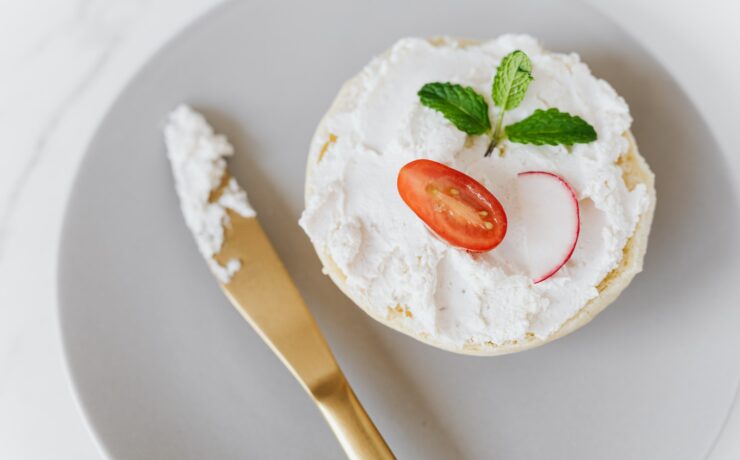 Vu du haut, une délicieuse tartinade de mascarpone sur du pain décoré de légumes et de menthe sur un plateau rond avec un couteau doré posé sur une table en marbre.