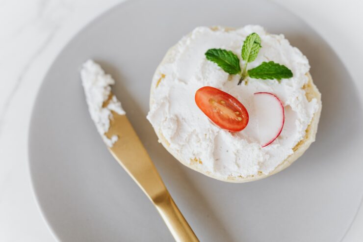 Vu du haut, une délicieuse tartinade de mascarpone sur du pain décoré de légumes et de menthe sur un plateau rond avec un couteau doré posé sur une table en marbre.