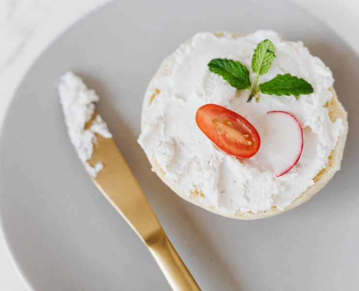 Vu du haut, une délicieuse tartinade de mascarpone sur du pain décoré de légumes et de menthe sur un plateau rond avec un couteau doré posé sur une table en marbre.