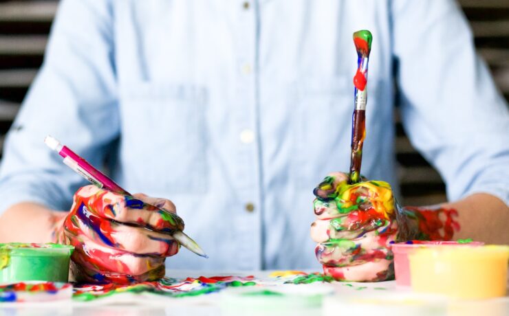 un homme avec ses mains sales avec des peintures colorées tient deux pinceaux